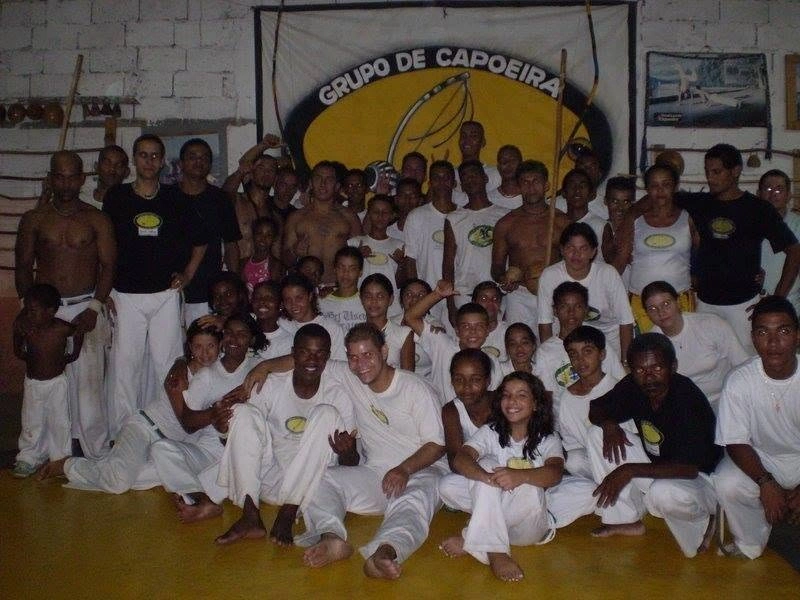 Foto de grupo com alunos de todas as idades diante da faixa do Grupo de Capoeira, nos primeiros anos da matriz